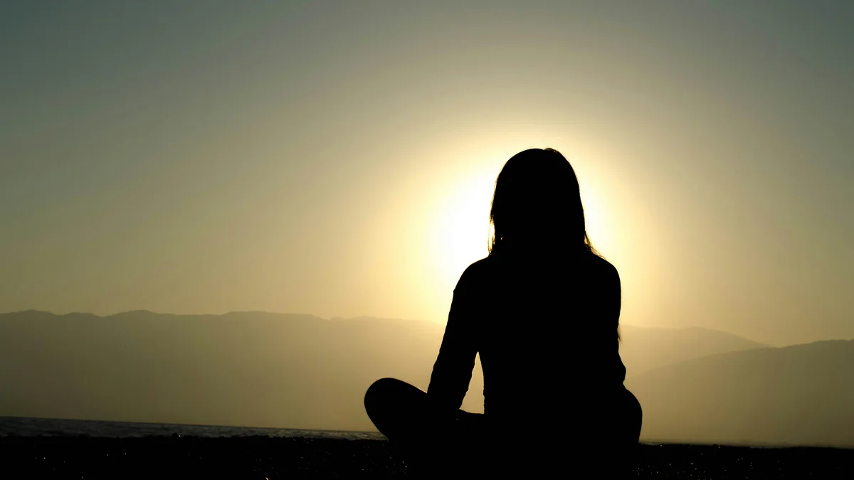 Silhouette en méditation face au soleil couchant au bord de l'eau - illustration de l'article Méditation Vipassana et bouddhisme Theravada : résumés d'enseignements (vidéos en anglais)